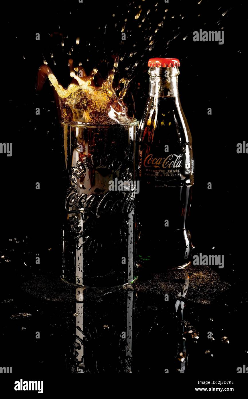 HELSINGBORG, SCHWEDEN - 06. APRIL 2022: Eine Studioaufnahme eines Eiswürfels, der in ein volles Glas Coca-Cola fällt, was zu einem Cola-Spritzer führt. Stockfoto