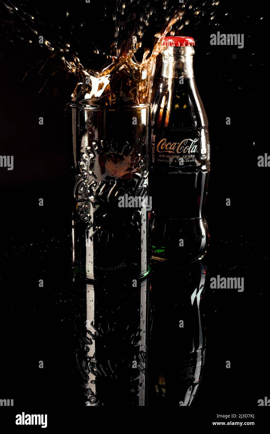 HELSINGBORG, SCHWEDEN - 06. APRIL 2022: Eine Studioaufnahme eines Eiswürfels, der in ein volles Glas Coca-Cola fällt, was zu einem Cola-Spritzer führt. Stockfoto