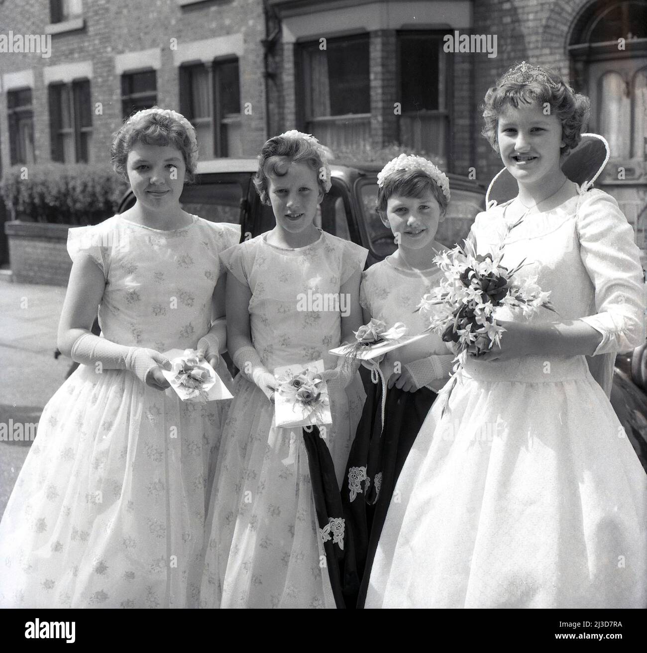 1961, historische Prozession am Maifeiertag, die lokale May Queen mit ihren jungen Mädchen, ihrem Gefolge, die alle ihre Blumenstrauß während der Frühlingsfeierlichkeiten am Maifeiertag halten, während sie für ein Foto stehen, draußen in einer Straße viktorianischer Reihenhäuser in Stockport, Manchester, England, Großbritannien. Stockfoto