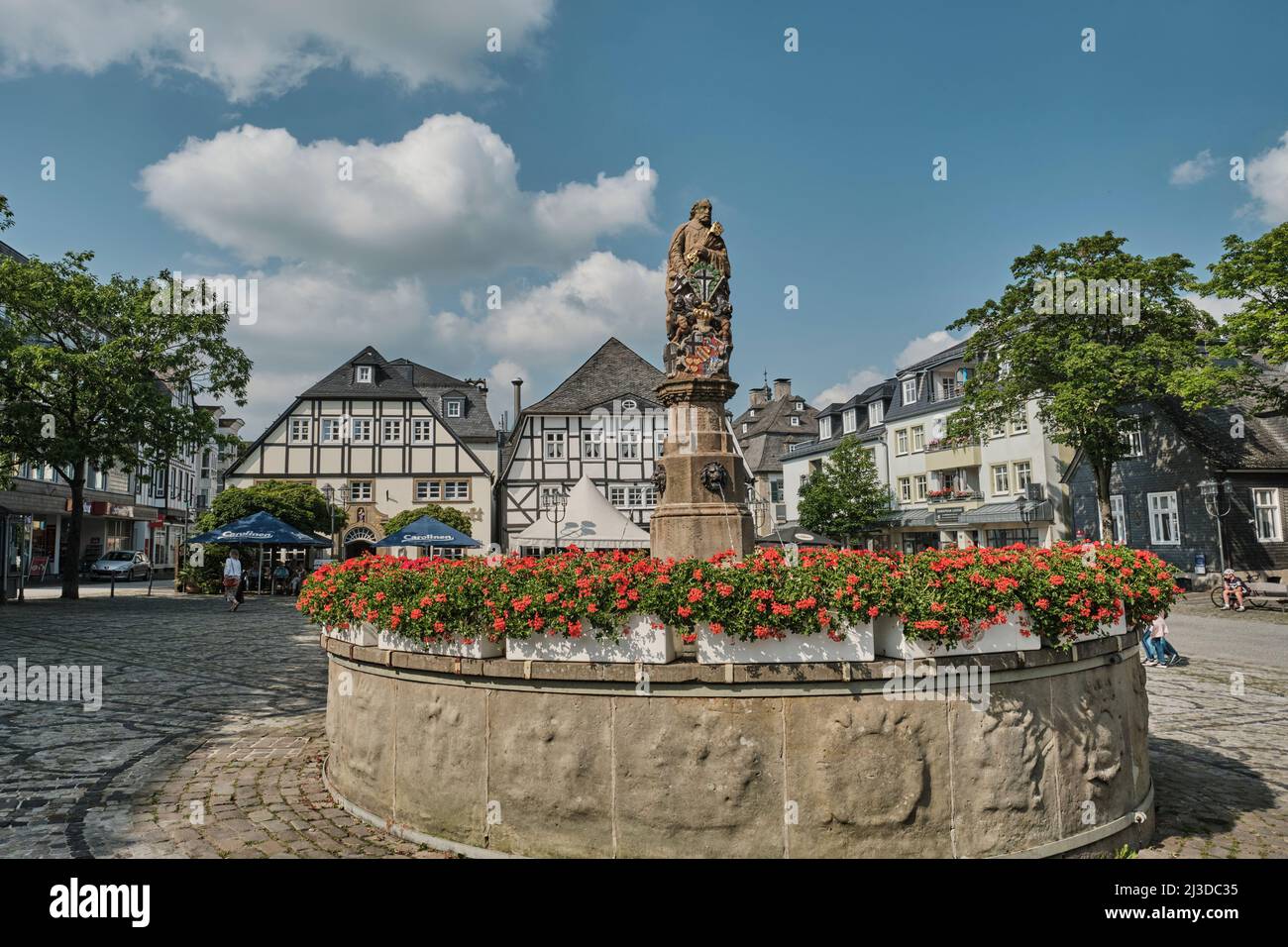 Alter Brunnen mit Skulptur im Stadtzentrum von Brilon mit mittelalterlichen Raumhäusern im Hintergrund Stockfoto