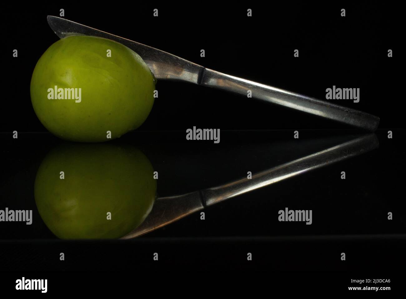 Ein silbernes Essmesser und Apfel reflektiert und isoliert auf Schwarzer Hintergrund Stockfoto