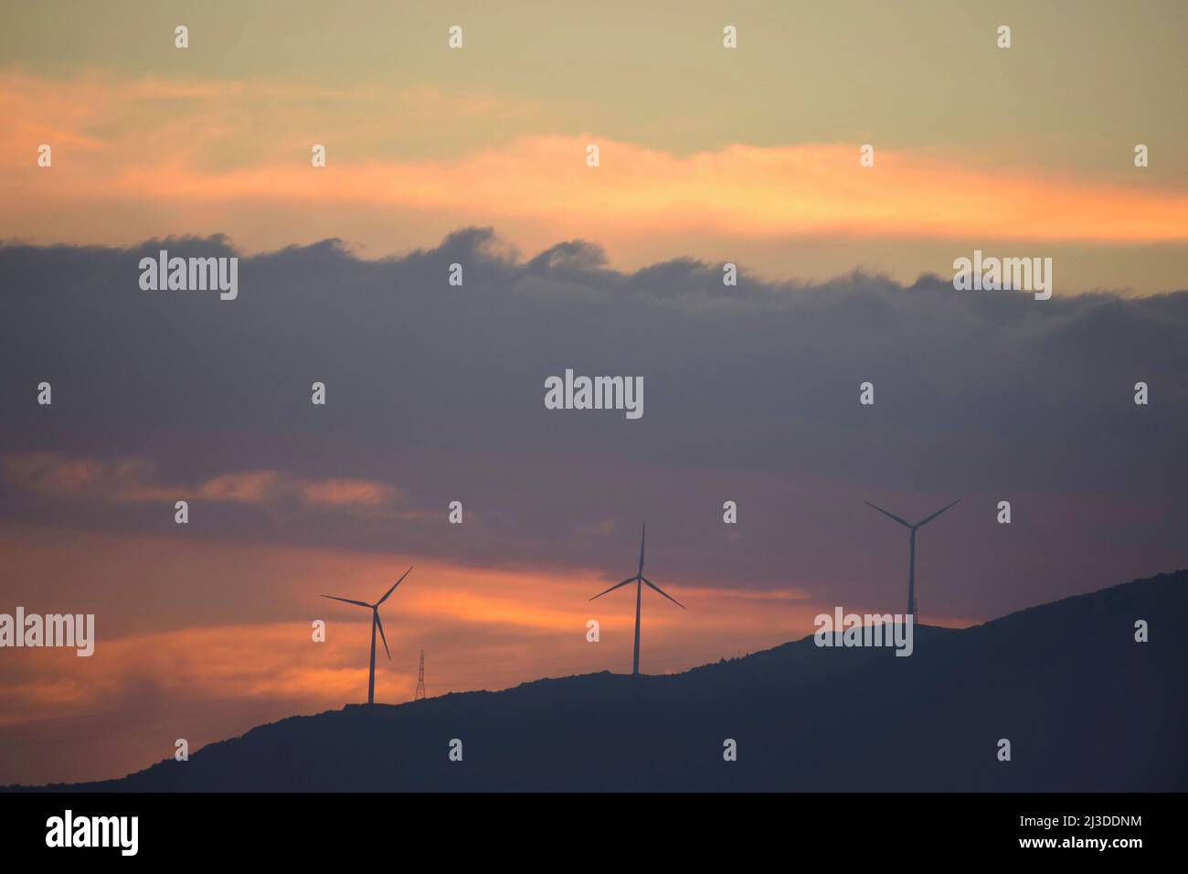 Luftturbinen auf einem Berg. Grüne Energie und Ökologie. Windturbinen und ein farbenfroher Sonnenuntergang mit Wolken in Griechenland Stockfoto