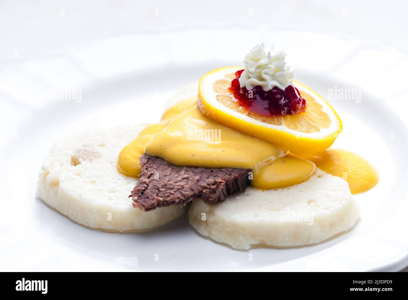 Sirloin-Sahnesauce mit Knödeln, serviert mit Zitrone, Preiselbeeren und Schlagsahne Stockfoto