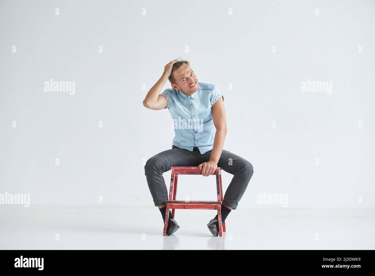 Brutaler Mann in einem Hemd mit kurzen Ärmeln, der auf dem Stuhl sitzt, seine Fäuste geballt, leicht gebeugt, unter dem Blick der Stirn Stockfoto