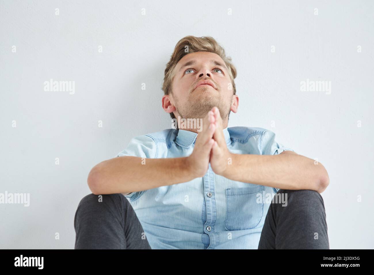 Brutaler Mann in einem Hemd mit kurzen Ärmeln auf dem Boden sitzend, seine Fäuste zusammengeballt, leicht gebeugt, unter dem Blick der Stirn Stockfoto