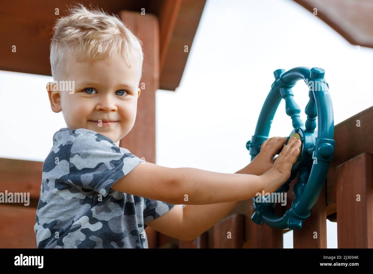 Glückliches Kind fährt auf einem Spielplatz ein Schiffsrad. Ein Kind, das Tarnung trägt, macht ein Signal für Boote in einem Spielhaus. Signalton. Kindheit voll Stockfoto