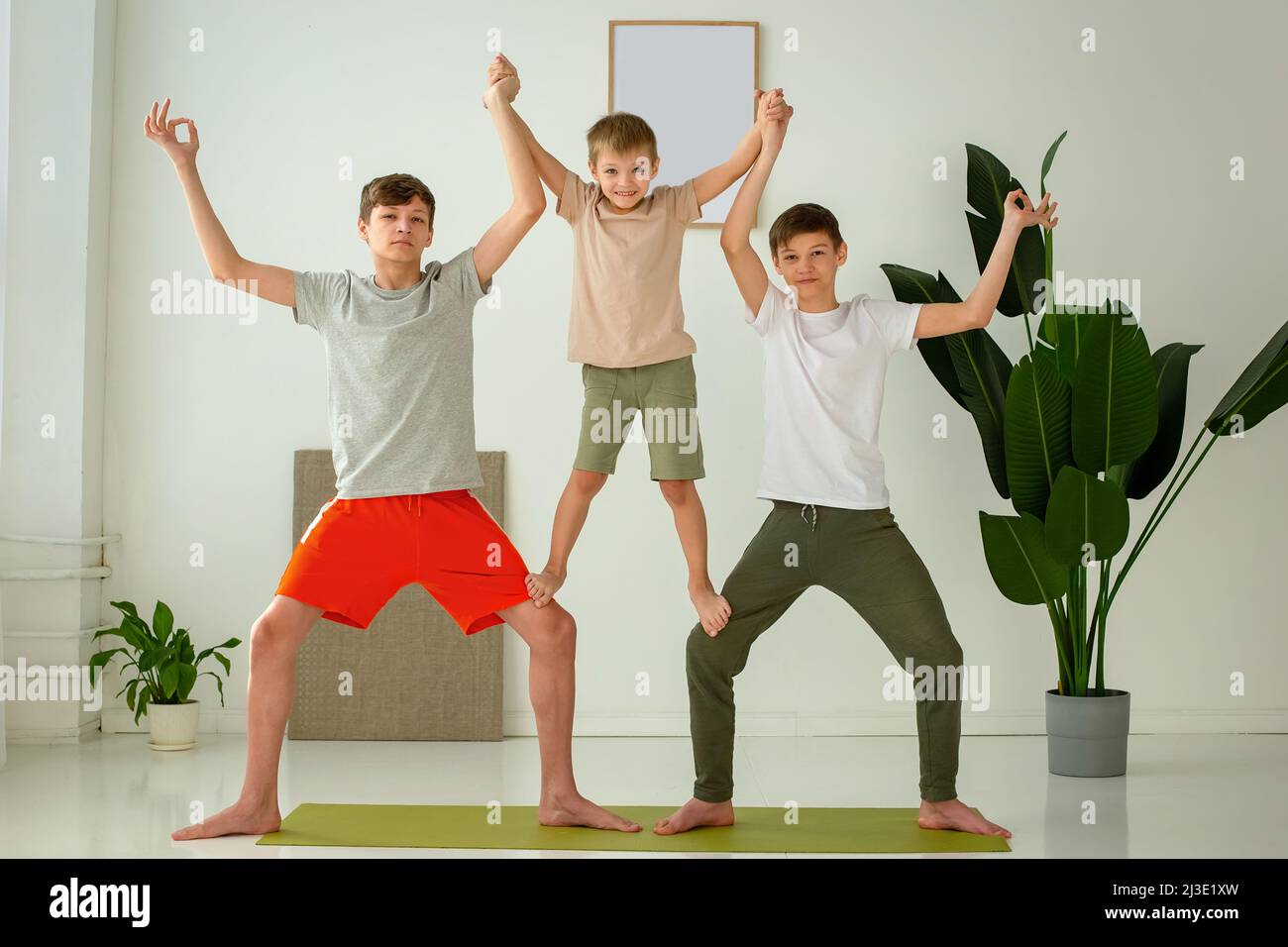 Ein glücklicher Junge und zwei Teenager führen mit Unterstützung Gruppenyogaübungen durch, während sie auf einer Sportmatte sitzen. Stockfoto