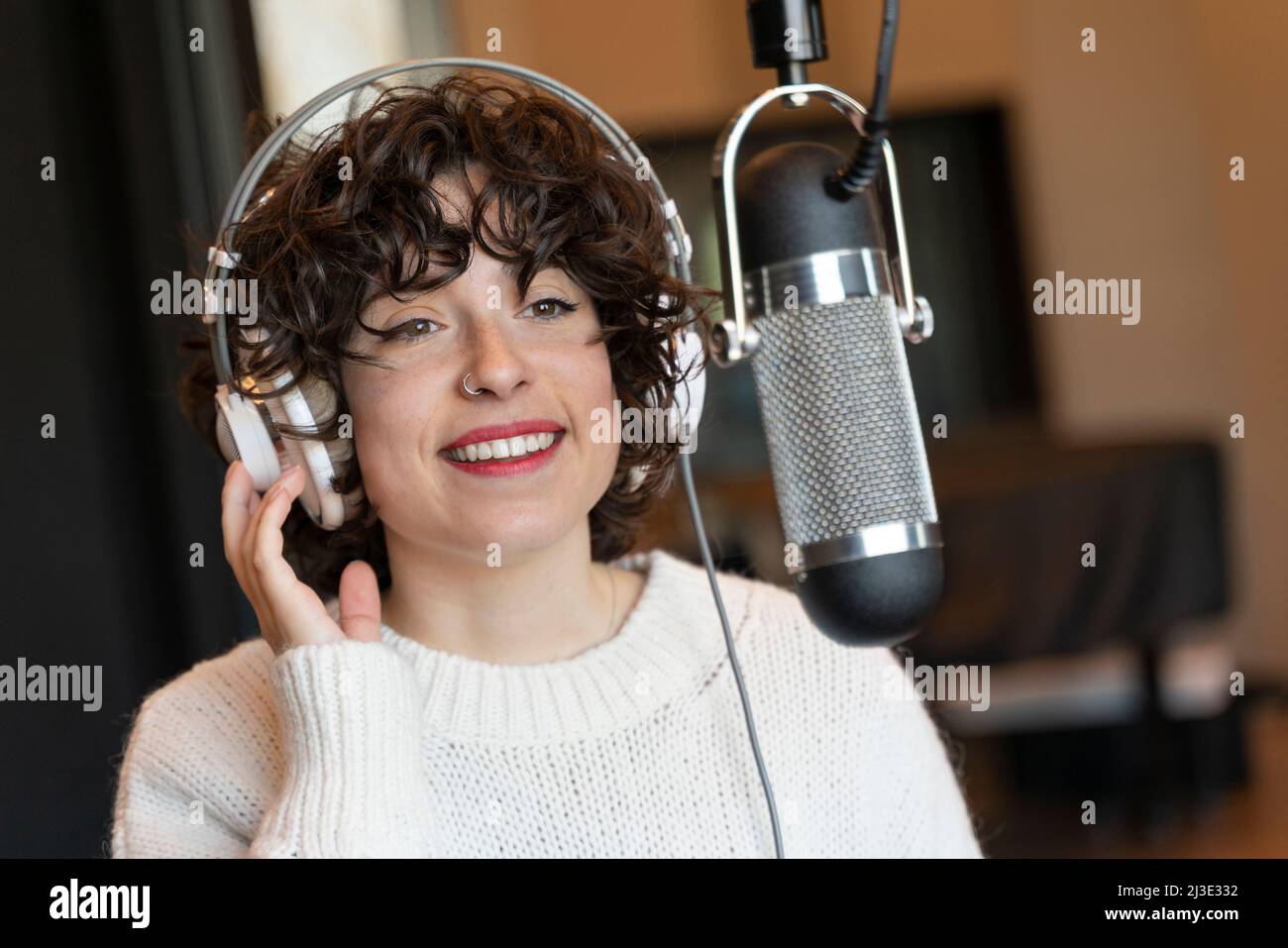Eine junge Sängerin mit lockigen Haaren, die in einem echten Studio einen Song aufzeichnete Stockfoto