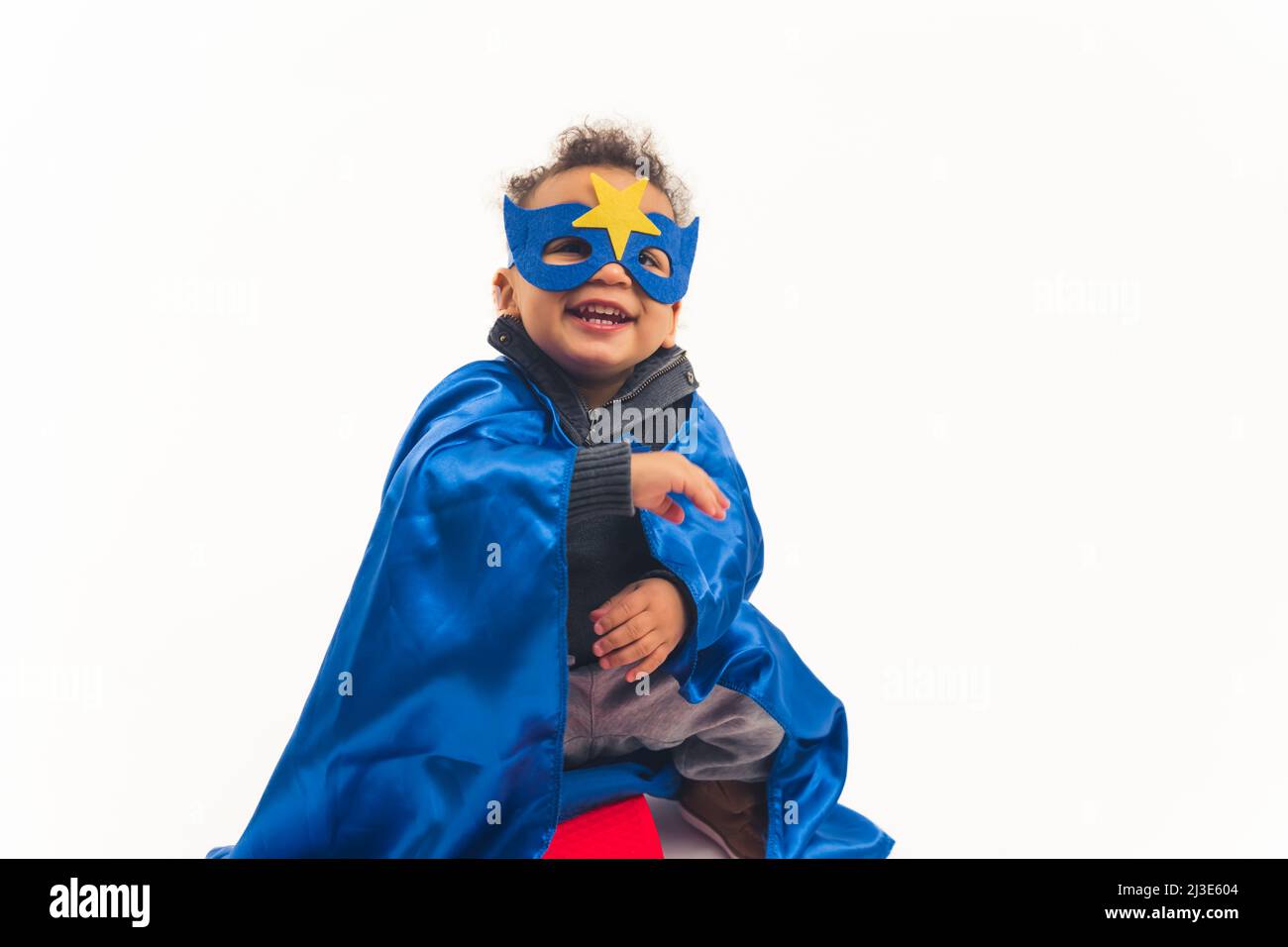 Kleiner afroamerikanischer lockiger Junge mit dem blauen Kostüm des Superhelden lachend voller Schuss Studio Schuss weißen Hintergrund Kopie Raum. Hochwertige Fotos Stockfoto