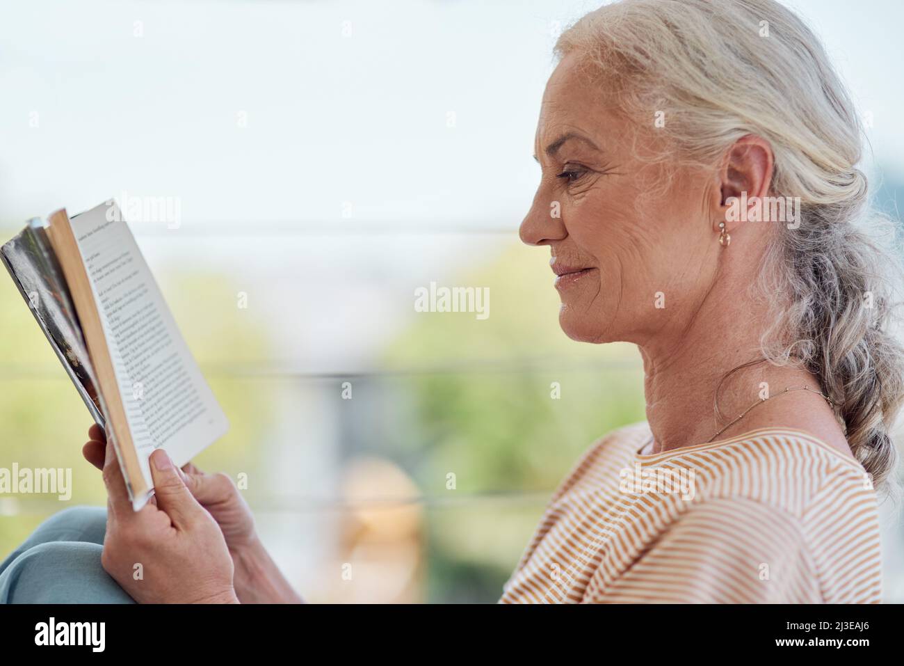 Weniger Stress, mehr lesen. Aufnahme einer reifen Frau, die zu Hause auf ihrem Balkon ein Buch liest. Stockfoto