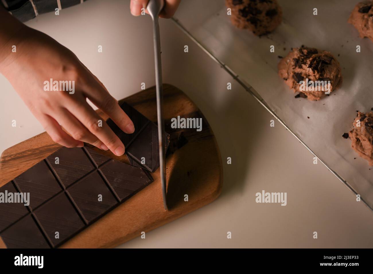 Draufsicht, weibliche Hände mit einem Messer schneiden eine Schokolade Bars auf einem Holz Schneidebrett, die Vorbereitung der Zutaten für das Backen von Schokolade Cookies. Stockfoto