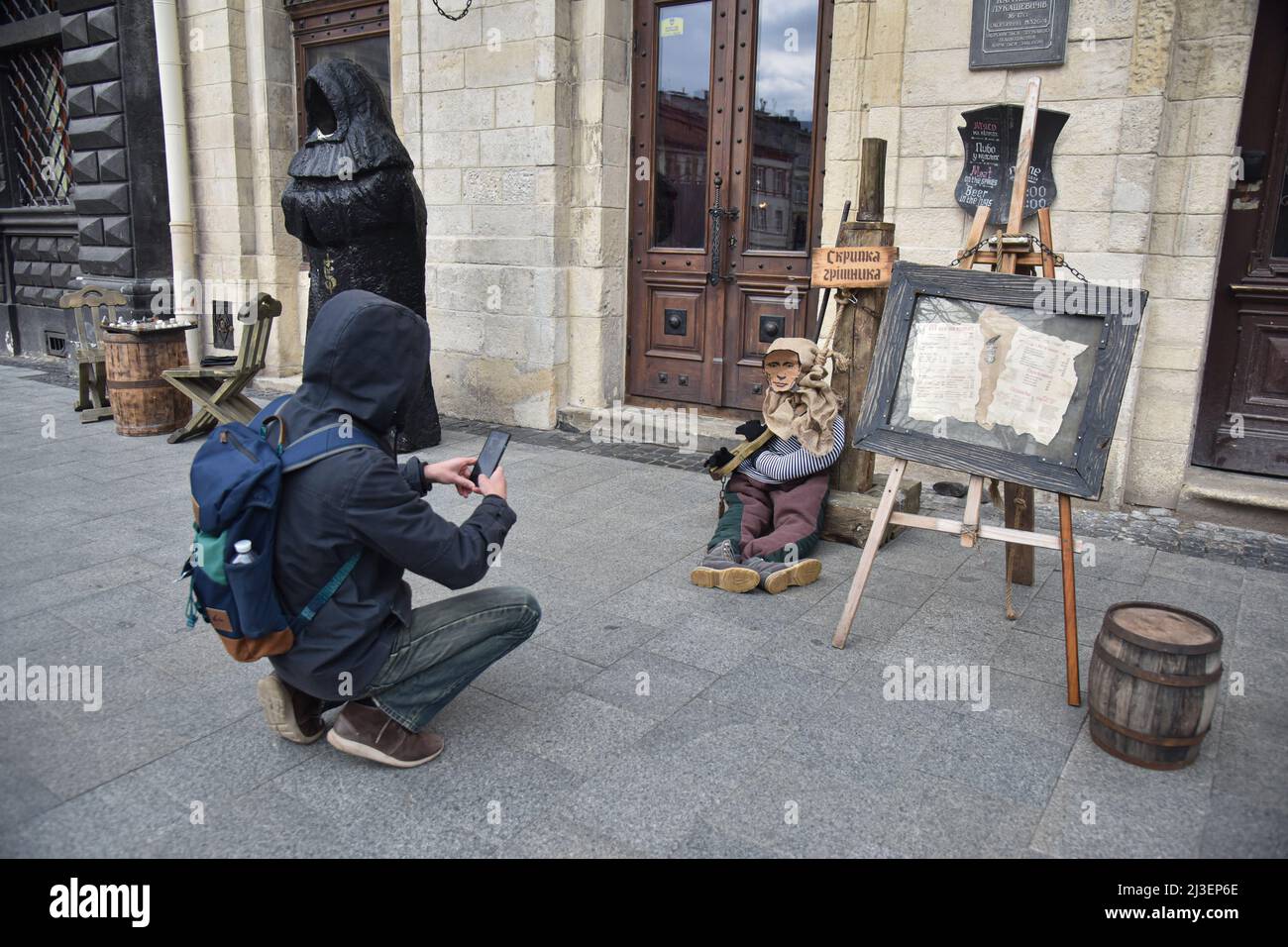 Lviv, Ukraine. 03. April 2022. Ein Mann fotografiert eine Schaufensterpuppe eines mittelalterlichen Gefangenen mit einem Porträt des russischen Präsidenten Wladimir Putin am Eingang eines Cafés in Lemberg. Aufgrund der militärischen Invasion Russlands in die Ukraine wurde eine Schaufensterpuppe eines mittelalterlichen Gefangenen mit dem Kopf der Besatzungsmacht, Präsident Wladimir Putin, in mittelalterliche Folter versetzt - "die Geige des Sünders" - in der Nähe des Cafés von Lviv platziert.Quelle: SOPA Images Limited/Alamy Live News Stockfoto