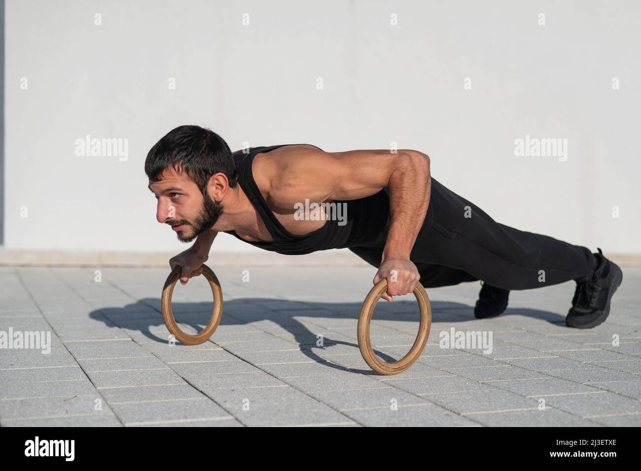 Ein Mann in schwarzer Sportkleidung, der im Freien Ring-Liegestütze macht  Stockfotografie - Alamy