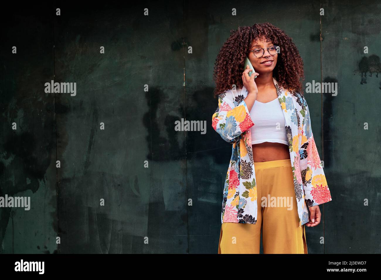 Junge afroamerikanische Frau mit lockigen Haaren, die ihr Mobiltelefon im Freien benutzt Stockfoto