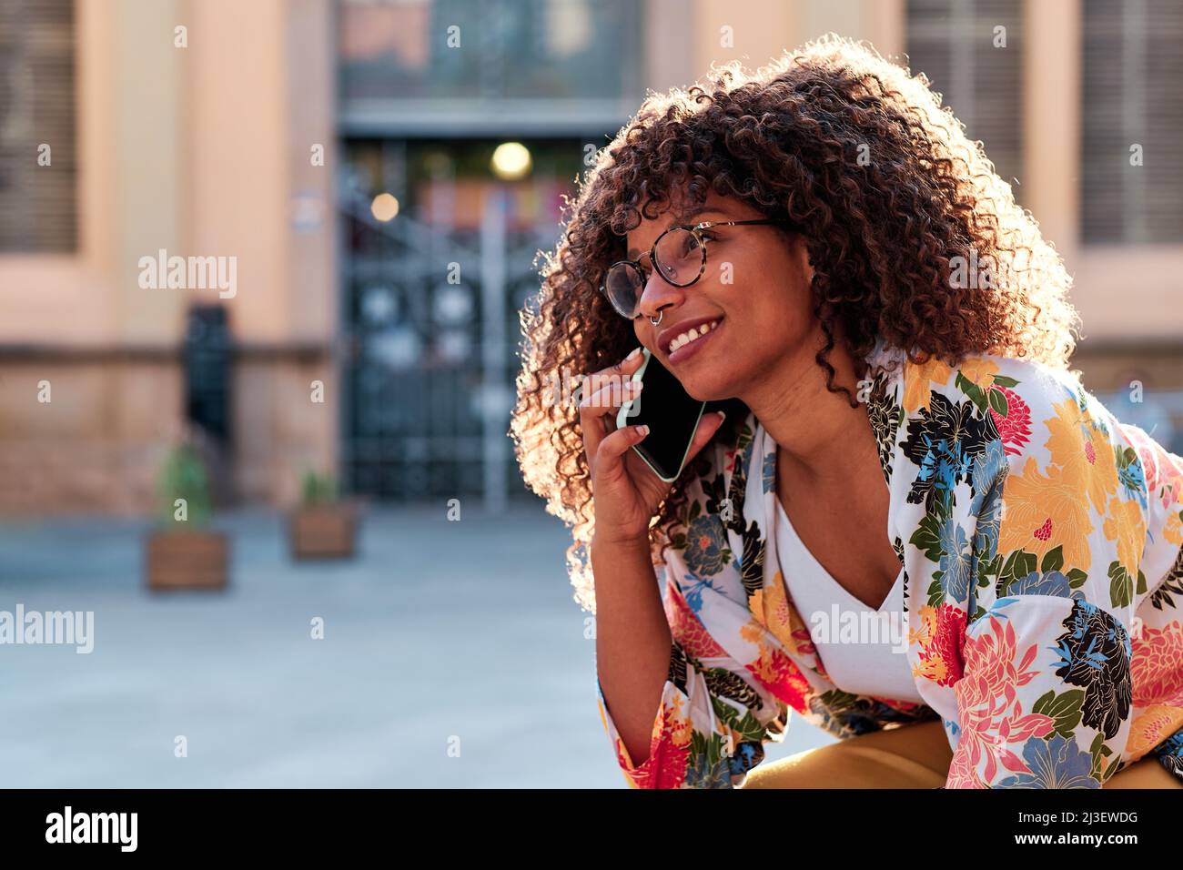 Junge afroamerikanische Frau mit lockigen Haaren, die ihr Mobiltelefon im Freien benutzt Stockfoto