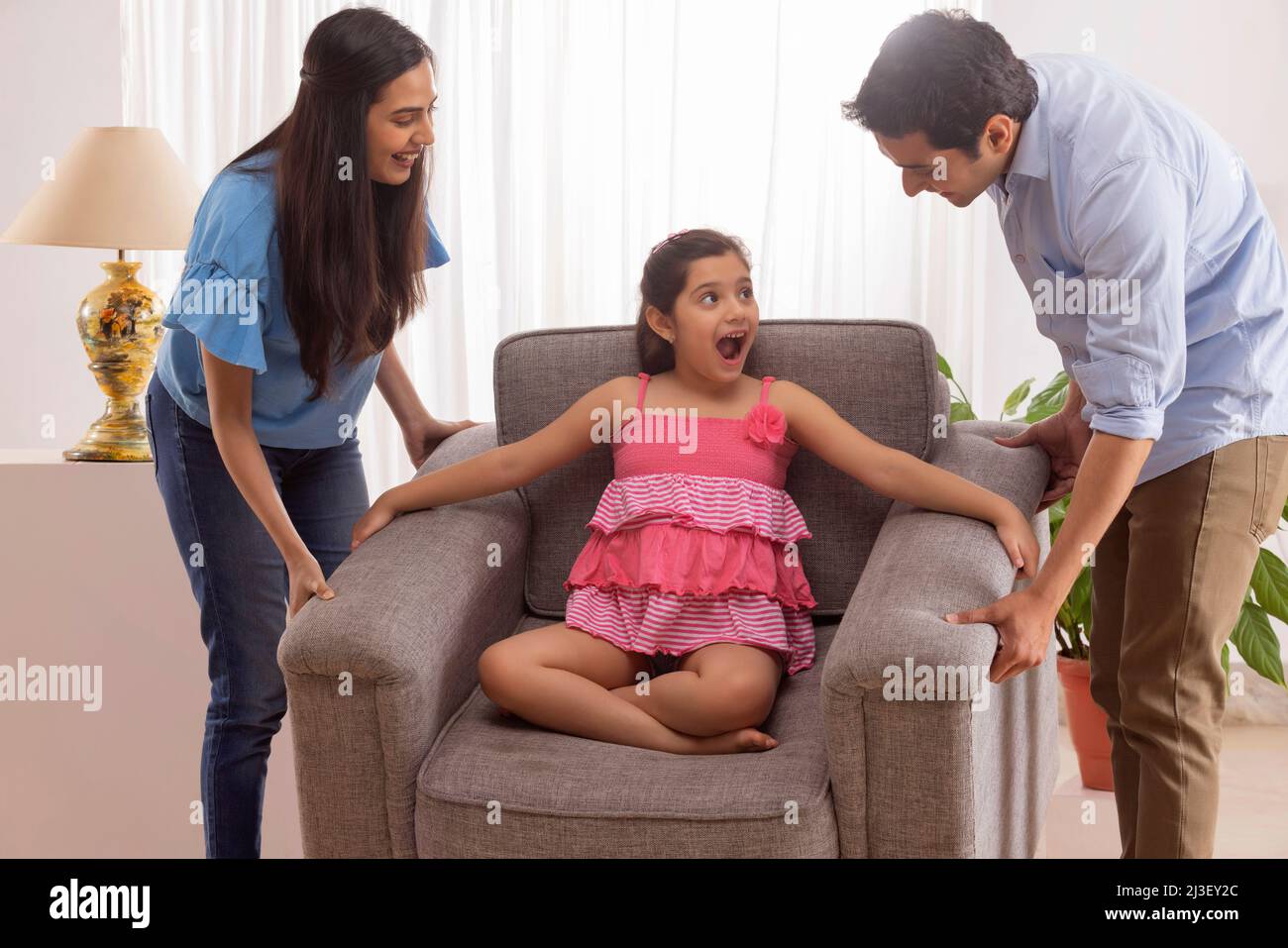 Eltern heben Sofa, während Tochter auf ihm sitzen Stockfoto