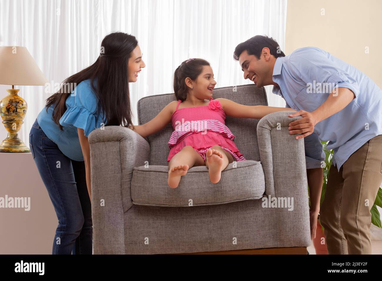 Eltern heben Sofa, während Tochter auf ihm sitzen Stockfoto