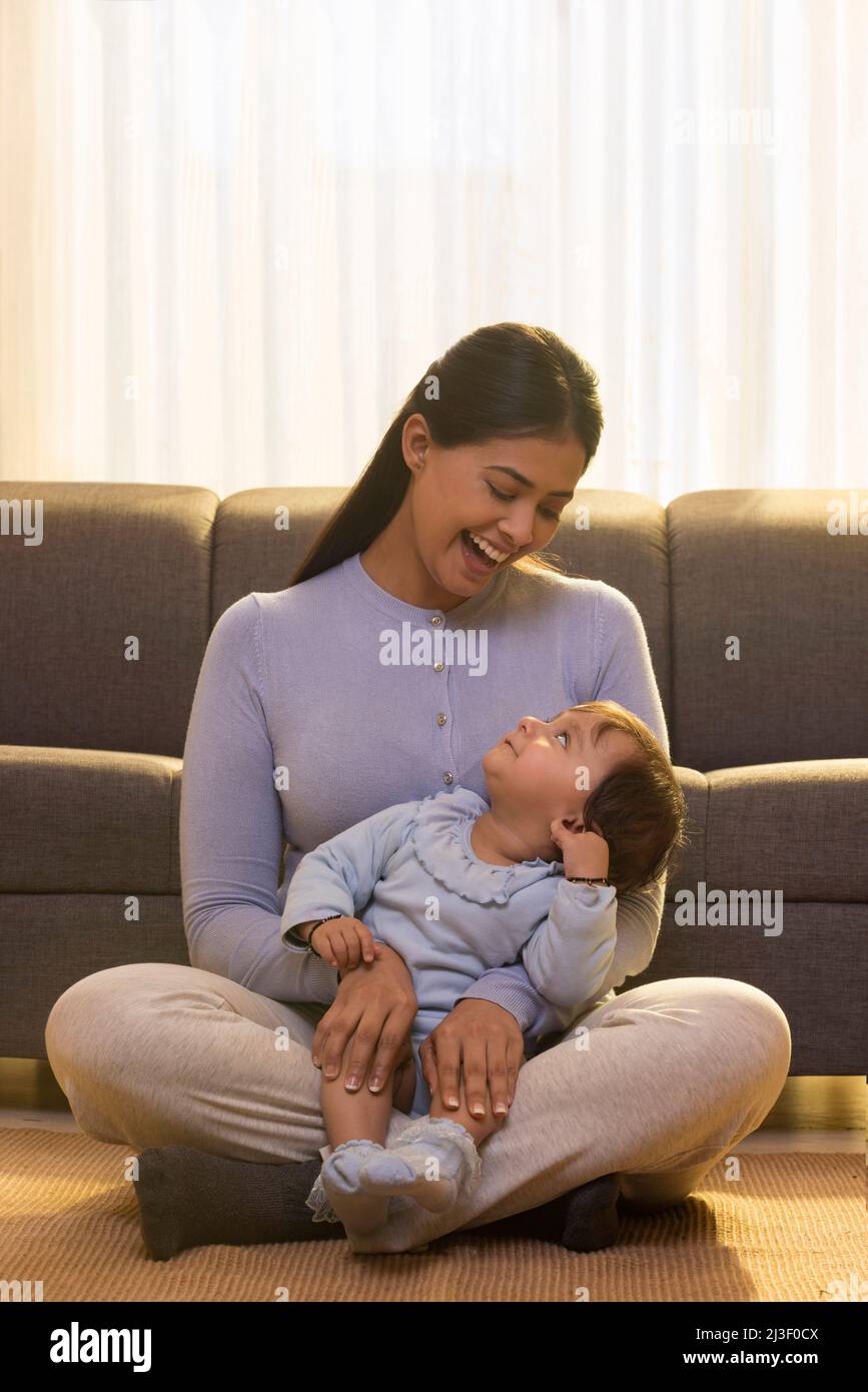 Niedliches Baby, das auf das Gesicht der Mutter schaut, während es auf dem Schoß sitzt Stockfoto