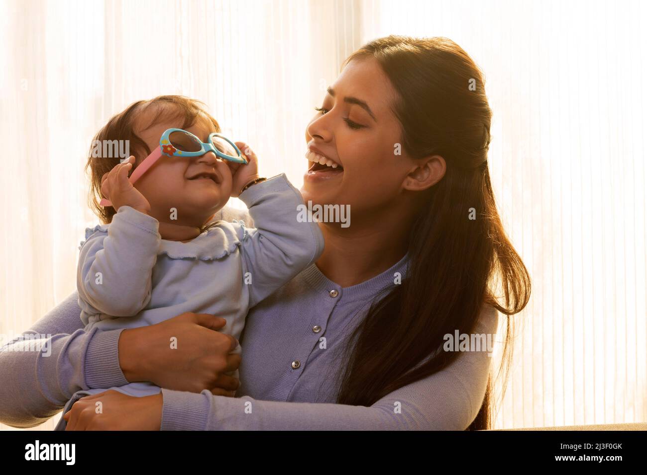 Mutter lacht, während das Baby eine Sonnenbrille trägt Stockfoto