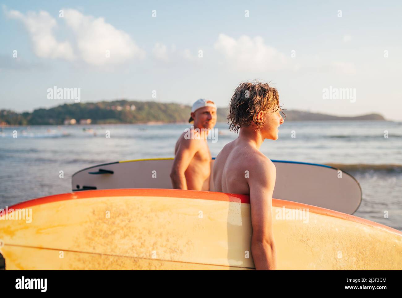 Teen boy mit Surfbrett gehen auf das Meer zum Surfen. Er hat einen Winterurlaub und genießt ein wunderschönes Sonnenuntergangslicht mit seinem Vater auf Sri Lanka. Fa Stockfoto