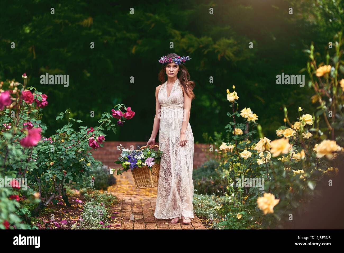 Folgen Sie dem Blumenpfad, um die besten Blumen zu pflücken. Aufnahme einer schönen jungen Frau, die einen Blumenkranz trägt und einen Korb voller Blumen in der Hand hält Stockfoto