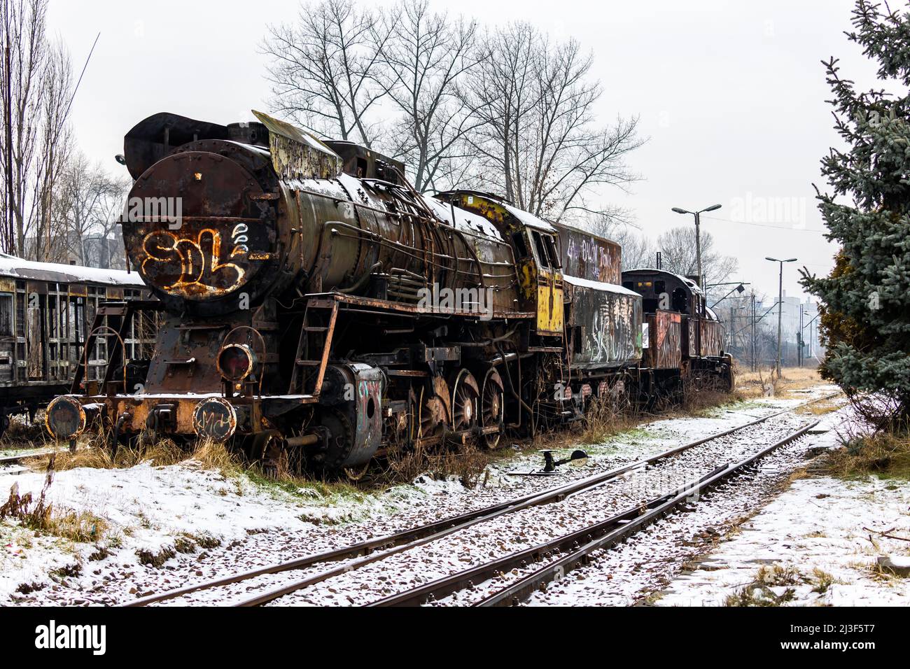 Alte, rostige, abgerissene Dampflokomotive, die auf der Seitenspur des Bahnhofs steht. Aufnahme an bewölktem Wintertag. Stockfoto