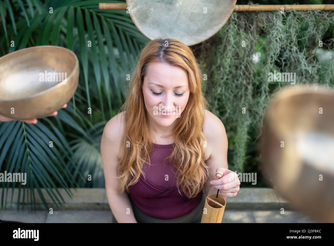 Yoga-Konzept, Meditation und Klangtherapie. Schöne junge kaukasische Frau, umgeben von tibetischen Klangschalen und Instrumenten aus Kupfer. Stockfoto
