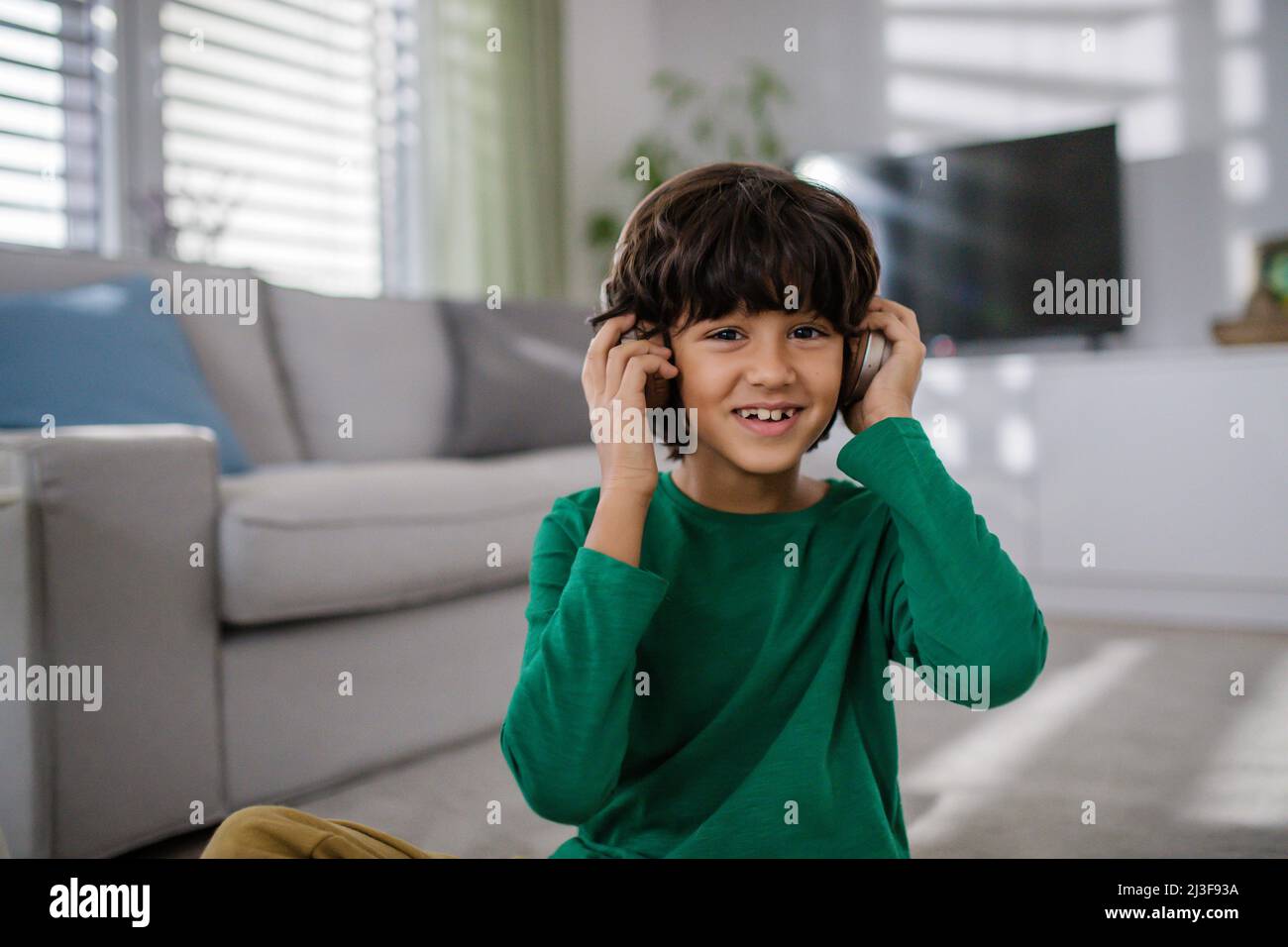 Fröhlicher, multirassischer Junge mit Kopfhörern, der zu Hause Musik hört. Stockfoto