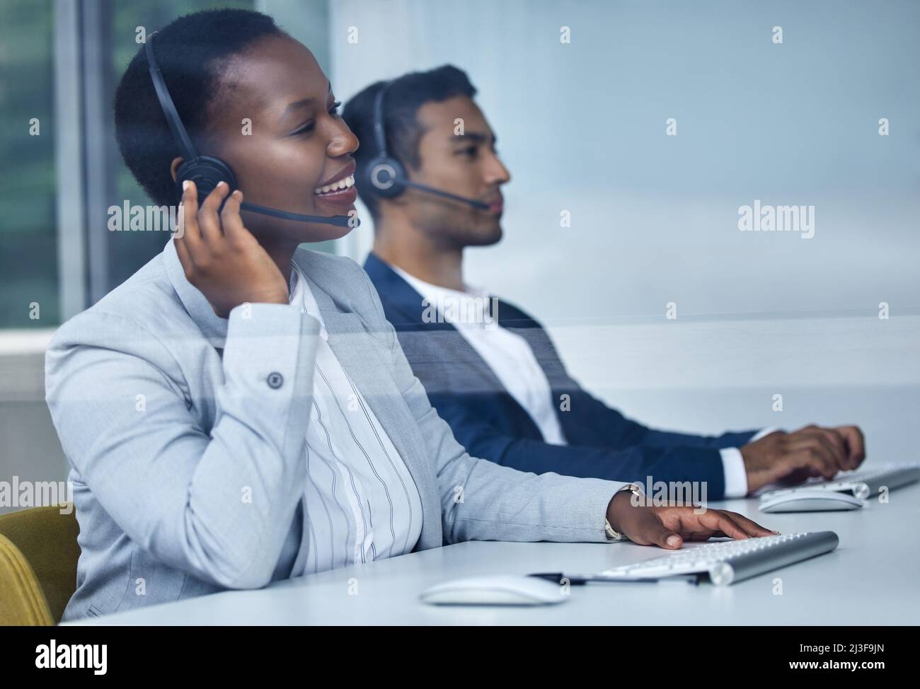 Hallo. Was kann ich heute für Sie tun? Eine kurze Aufnahme von zwei jungen Callcenter-Agenten, die an ihren Schreibtischen im Büro arbeiten. Stockfoto