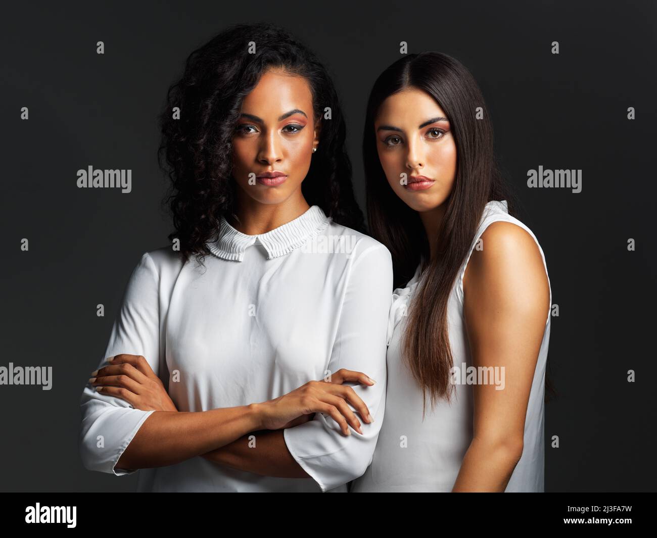 Strahlende natürliche Schönheit. Porträt zweier attraktiver junger Frauen in weißen Blusen, die eng zusammen vor dunklem Hintergrund im Studio posieren Stockfoto