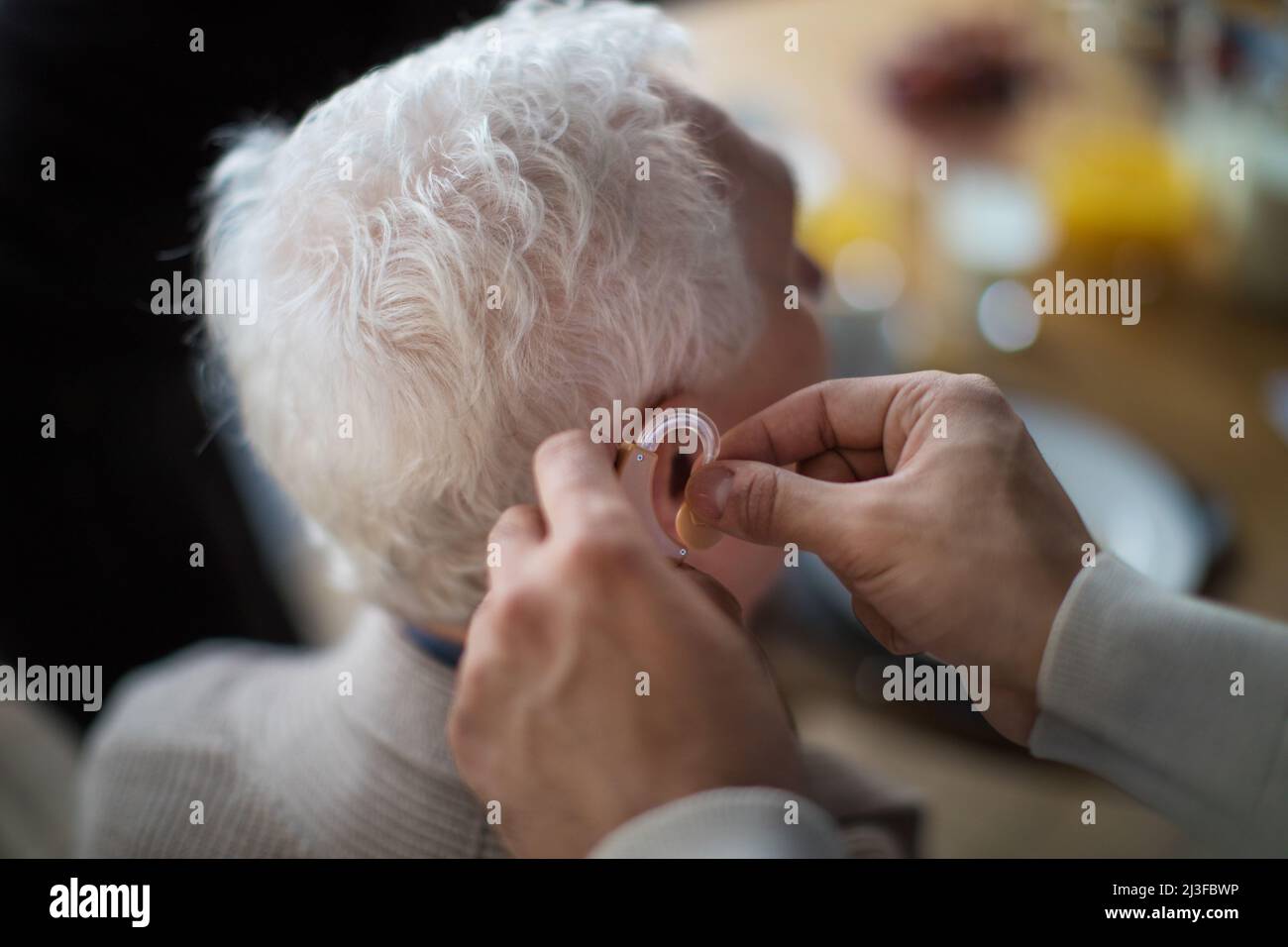 Nahaufnahme der Hand des Pflegepersonals, die ein Hörgerät in das Männerohr des Senioren einführt. Stockfoto