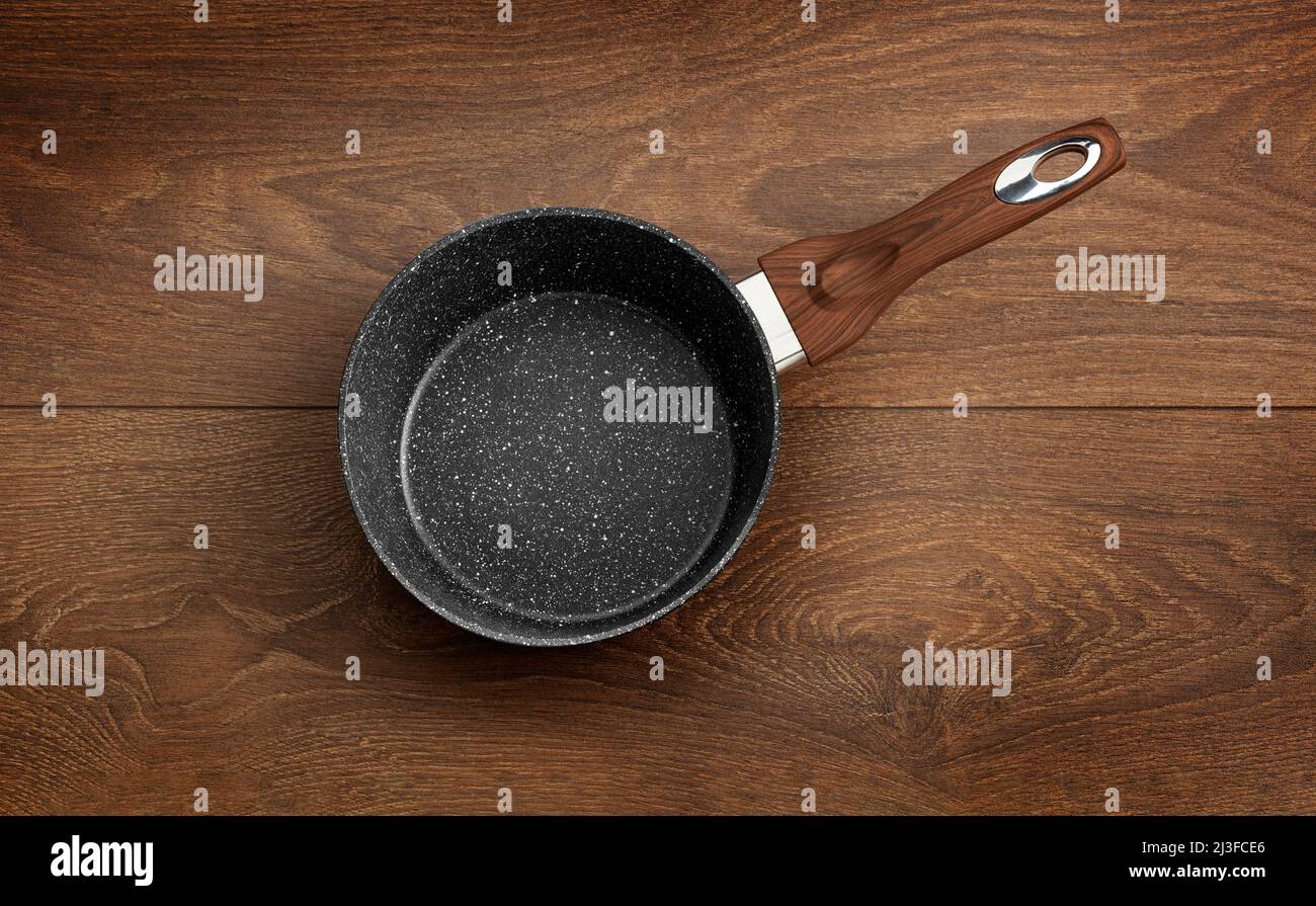 Moderne Bratpfanne mit Antihaftbeschichtung aus Granit, isoliert auf einem Hintergrund aus Holz. Stockfoto