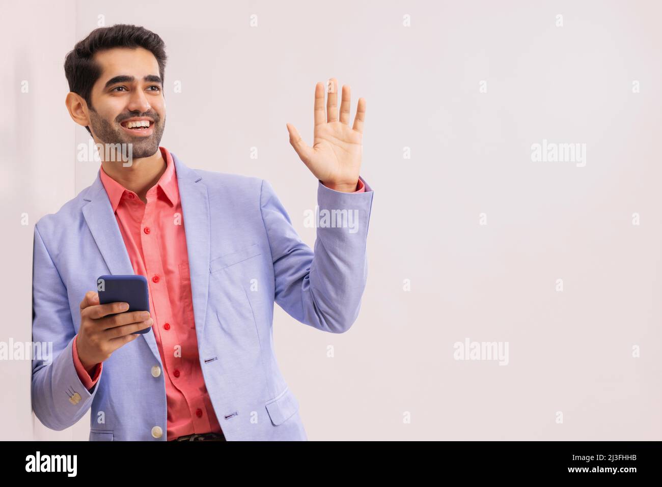 Junger Geschäftsmann im formellen Outfit, der mit einem Smartphone an anderer Stelle gestikuliert Stockfoto