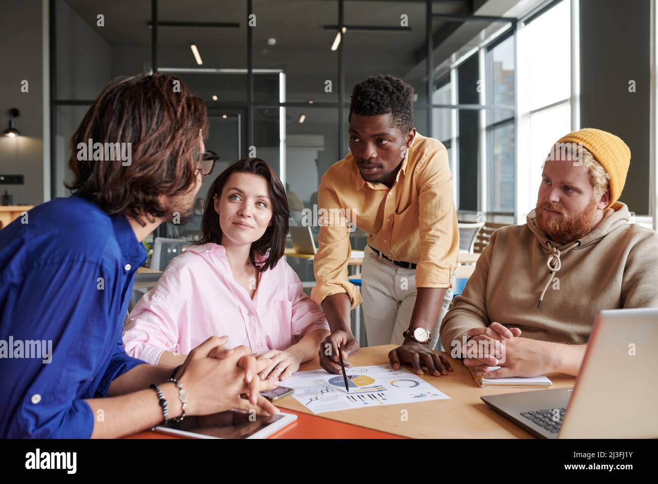 Gruppe junger interrassischer Kollegen, die sich den Bericht ansehen und analytische Daten bei einem Treffen im Büro diskutieren Stockfoto
