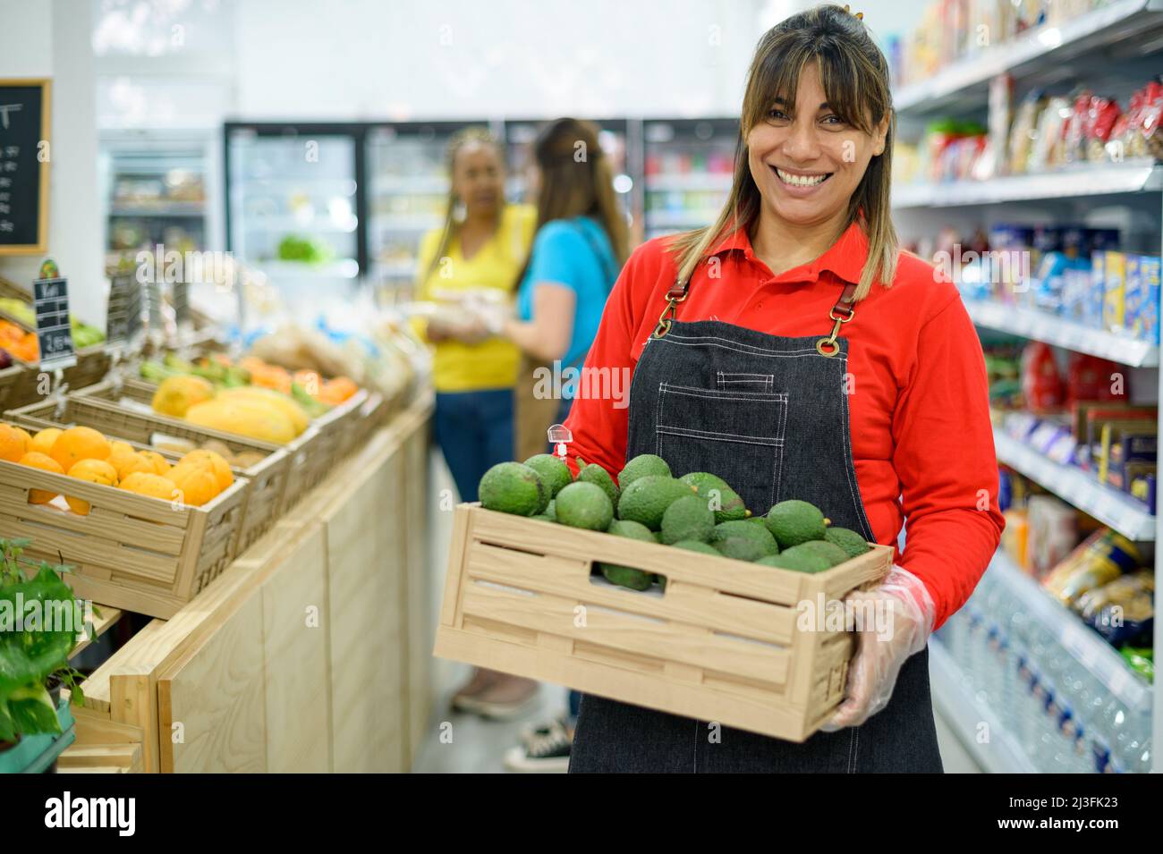 Glückliche ethnische Verkäuferin mit Schachtel Avocado im Supermarkt Stockfoto