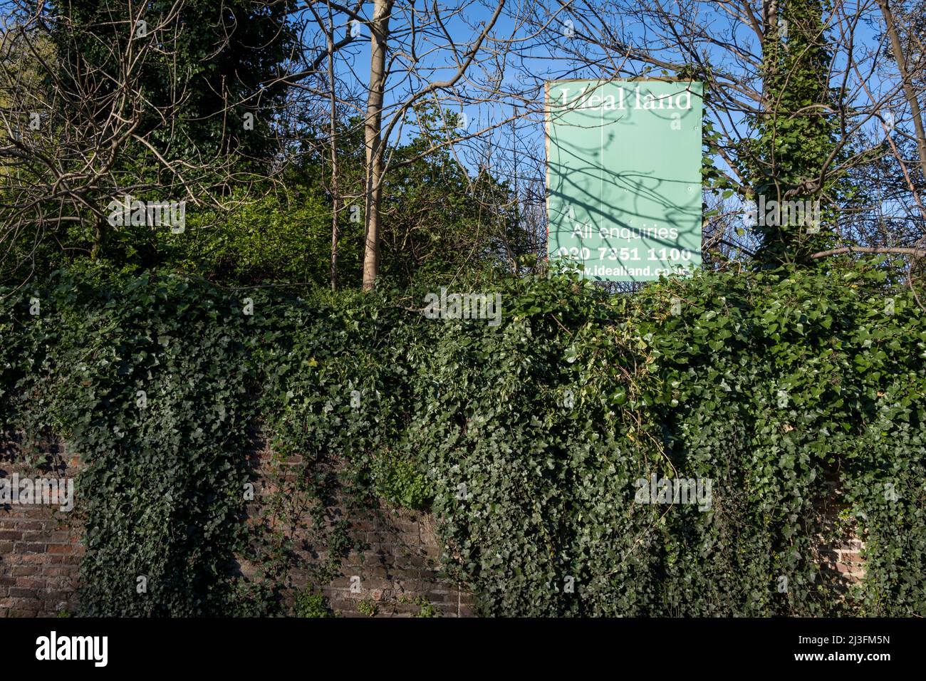 Ein Plakat für den Immobilienmakler „Ideal Land“ ist über einem von Mauern umgebenen Grundstück in Dulwich Village, Southwark, am 2.. April 2022 in London, England, zu sehen. Stockfoto