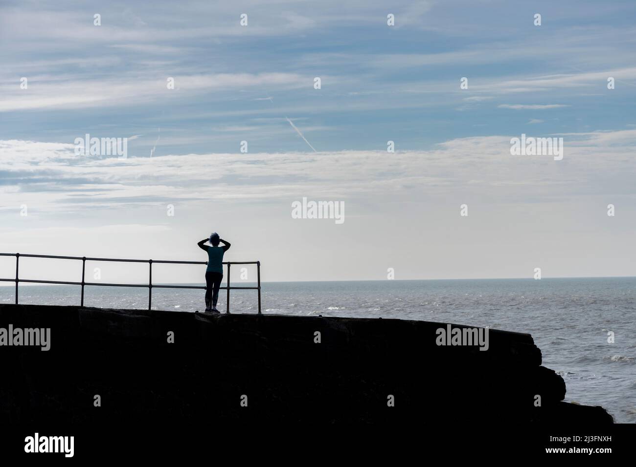 Silhouette einer Frau, die auf das Meer blickt und nach Schiffen sucht Stockfoto