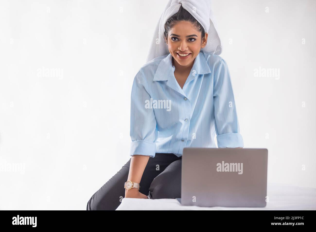 Junge Geschäftsfrau mit nassem Haar in einem Handtuch gewickelt, die auf dem Bett sitzt und sich anderweitig umsieht Stockfoto