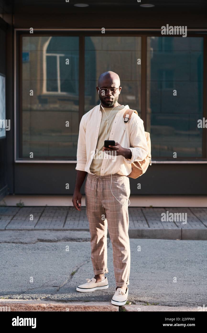 Serious junger schwarzer Mann in Sonnenbrille trägt modische Straße Outfit mit gps-Navigation auf dem Telefon in der Großstadt Stockfoto