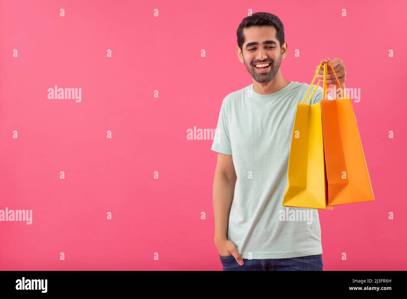 Glücklicher junger Mann, der mit Einkaufstaschen und Hand in der Tasche steht Stockfoto