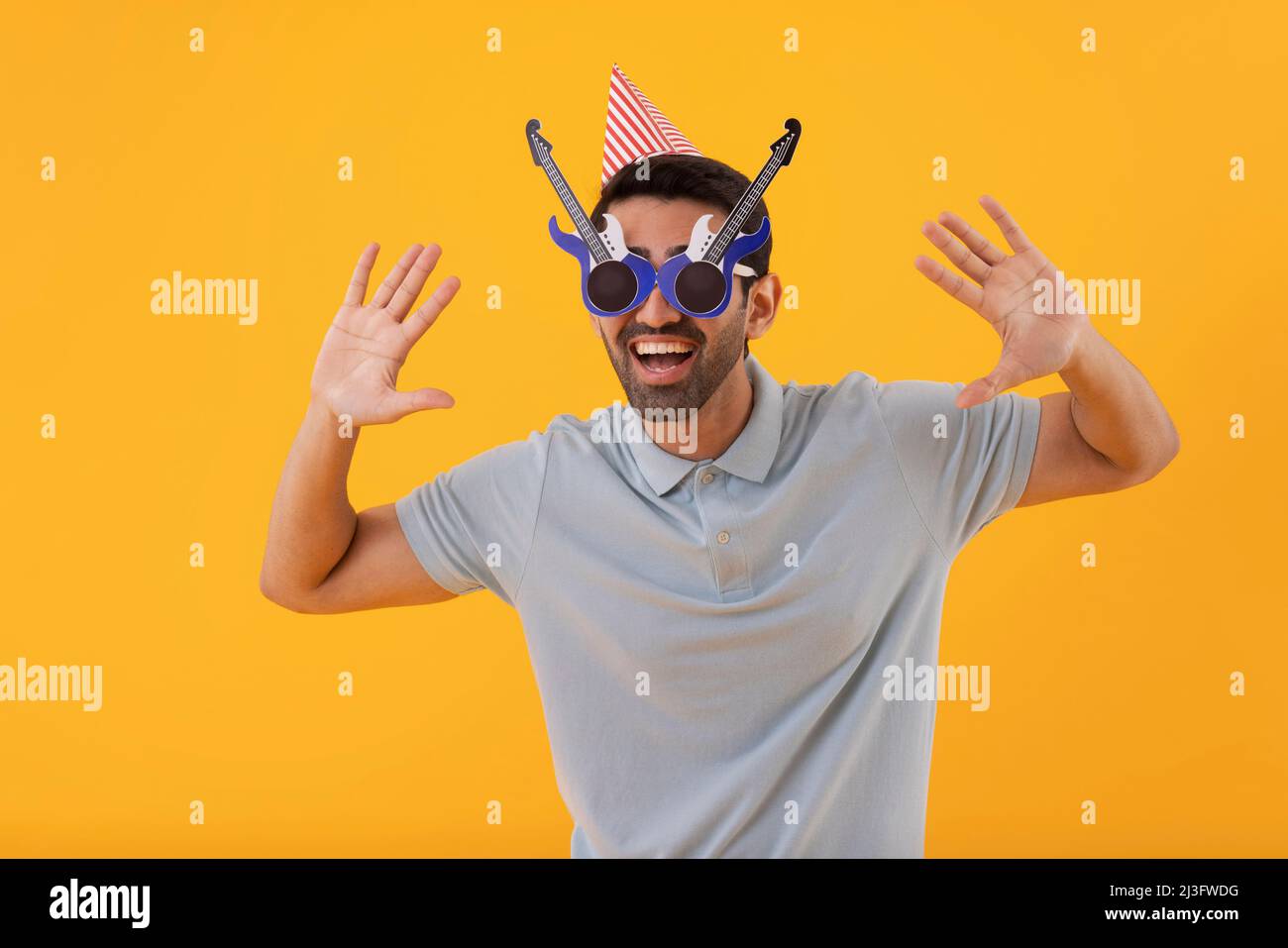 Lustiger junger Mann, der eine gitarrenförmige Augenbrille mit Partyhut trägt Stockfoto