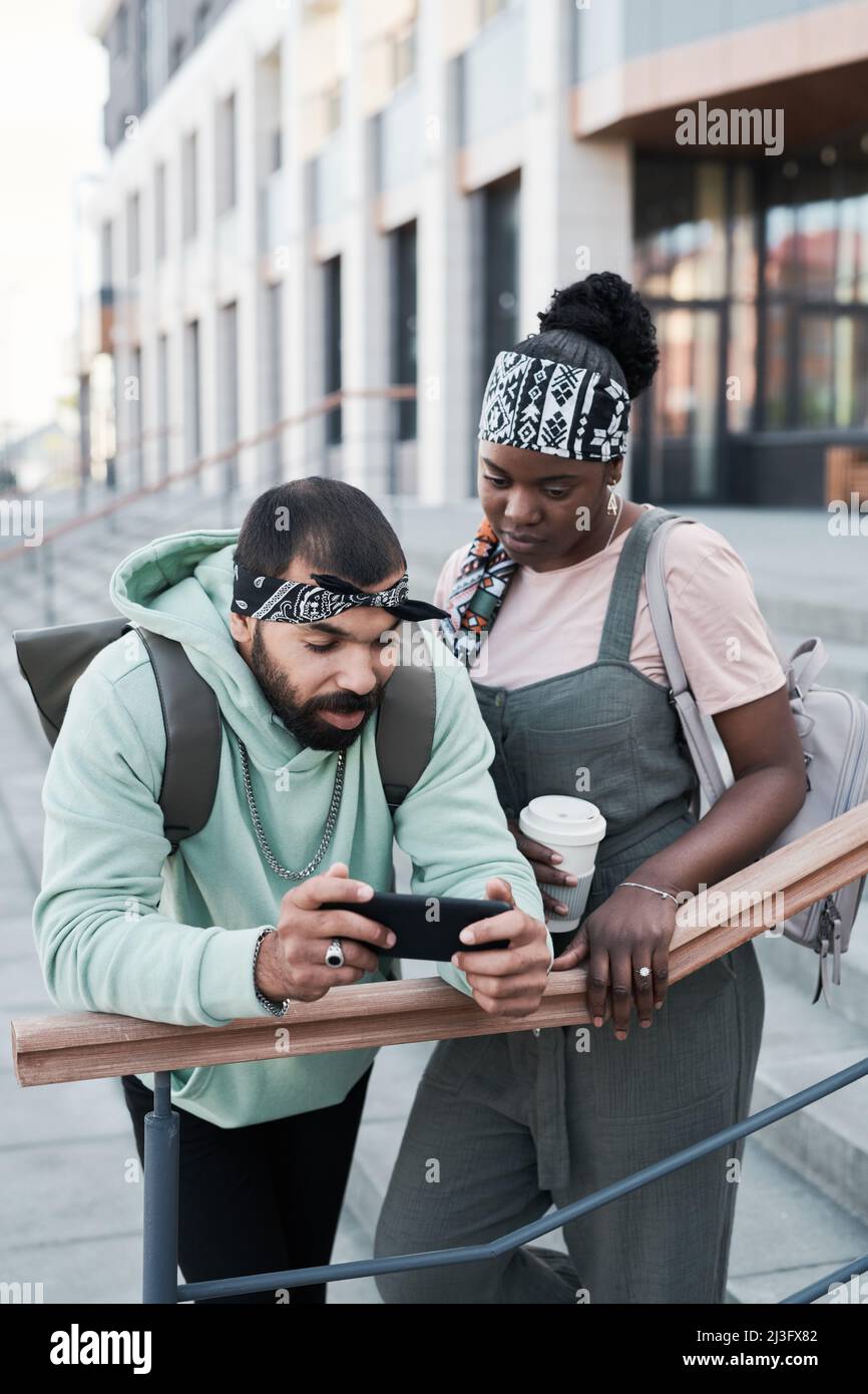Junge multiethnische Freunde, die sich in der Stadt am Geländer anlehnen und Videos auf dem Smartphone ansehen Stockfoto