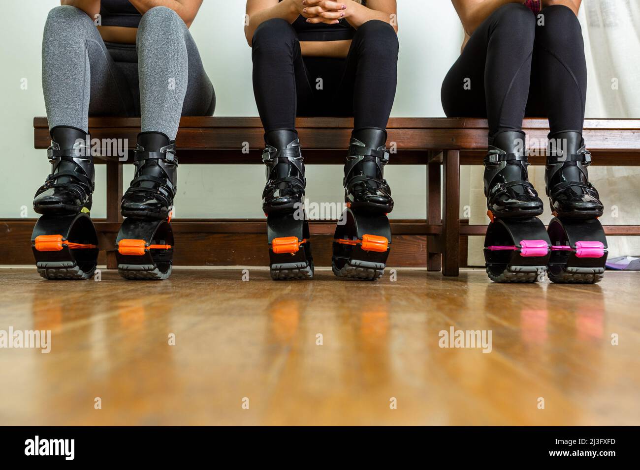 Sportlerinnen in Sportbekleidung und Sprungschuhen sitzen auf der Bank und ruhen sich während der Pause beim Fitnesstraining im Fitnessstudio aus Stockfoto