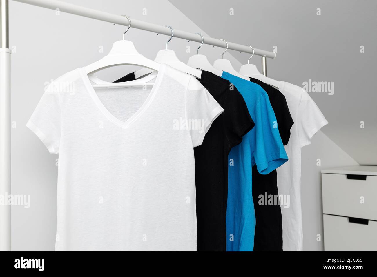 Eine Gruppe von verschiedenen T-Shirts, die an weißen Kleiderbügeln hängen. Kleiderständer. Vorlage, Modell. Stockfoto