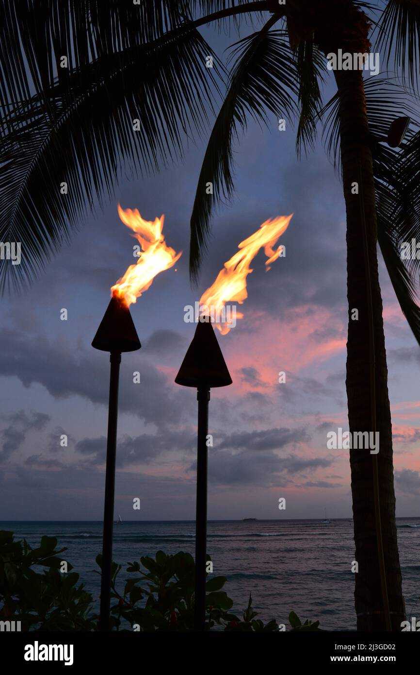 Traditionelle hawaiianische Fackeln brennen entlang der Küste von Waikiki Beach und werden von Palmen eingerahmt Stockfoto