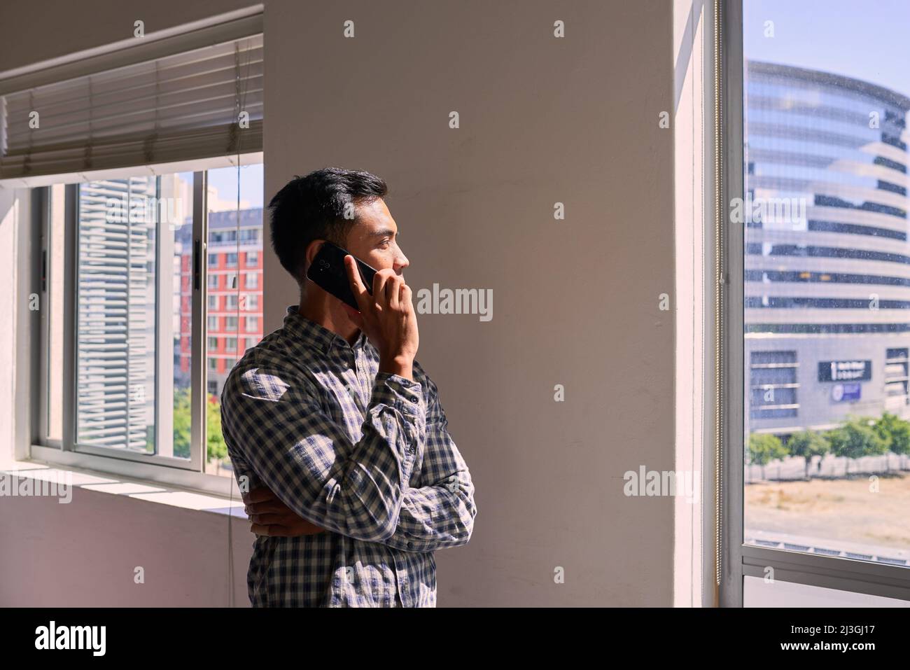 Eine breite Aufnahme eines Geschäftsmannes am Telefon, der vom Büro aus die Stadt ansah Stockfoto