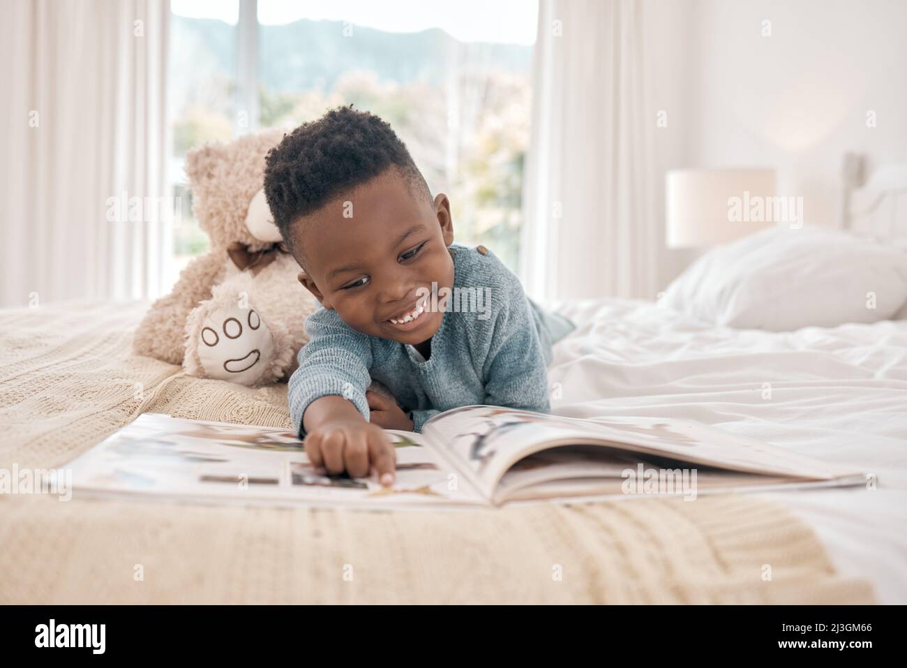 Er liest gern. Die ganze Aufnahme eines entzückenden kleinen Jungen, der zu Hause ein Buch auf einem Bett liest. Stockfoto