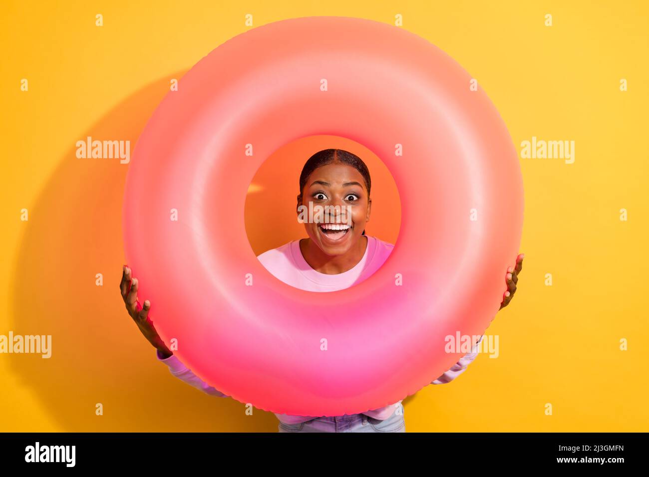 Foto von aufgeregt funky Mädchen halten aufblasbare Ring Gesicht Kopf schauen Kamera isoliert auf gelbem Hintergrund Stockfoto