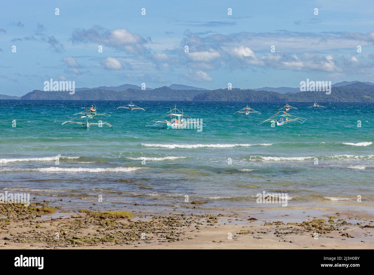 Philippinen, Palawan, Sabang Beach, Sandstrand, türkisfarbenes Meer und Kanus zum Angeln Stockfoto