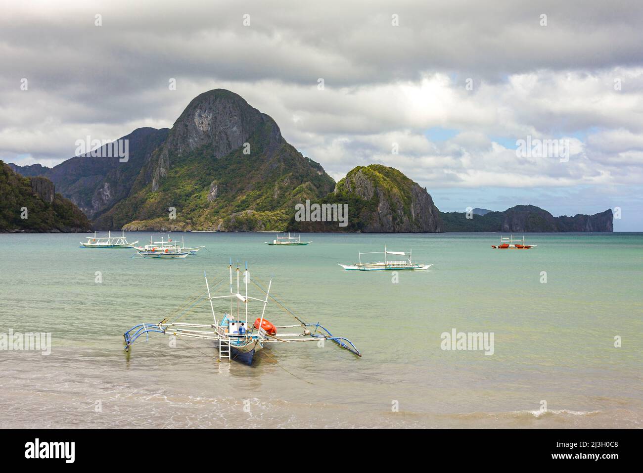 Philippinen, Palawan, El Nido, Kanus am Strand und felsige Insel im Hintergrund Stockfoto